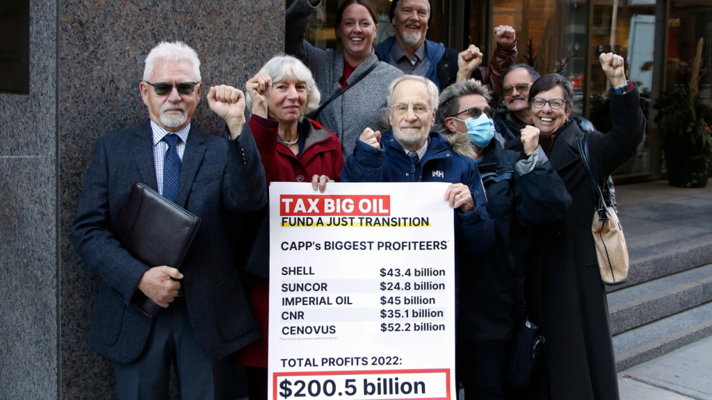 A photo of climate activists dressed as officials from the Ministry of Just Transition holding a Tax Big Oil poster